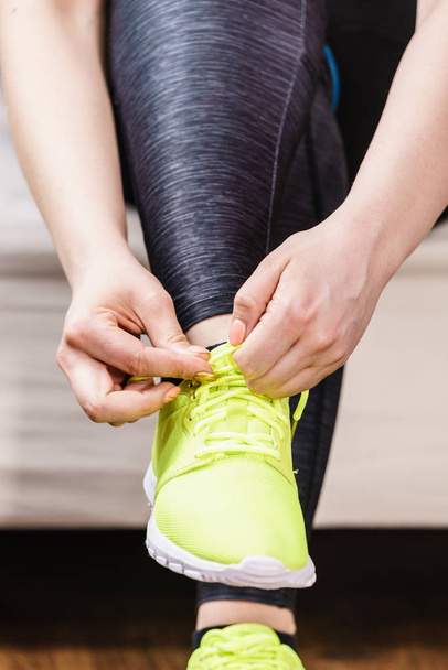 Woman in sportswear sitting on sofa indoor getting ready for exercises. Tying up shoes - Foto, Imagem