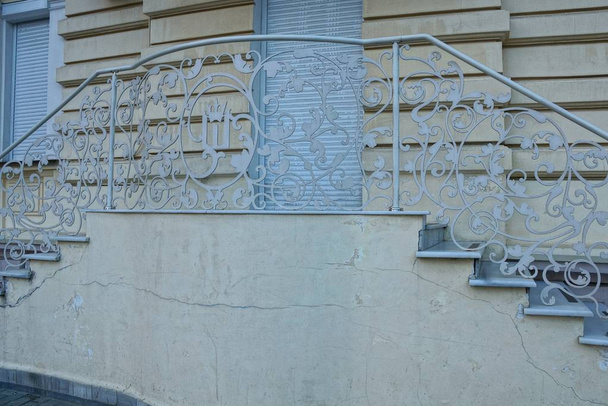 Braune Betonschwelle mit Stufen und eisengrauem Handlauf mit geschmiedetem Muster in der Straße nahe der Mauer - Foto, Bild