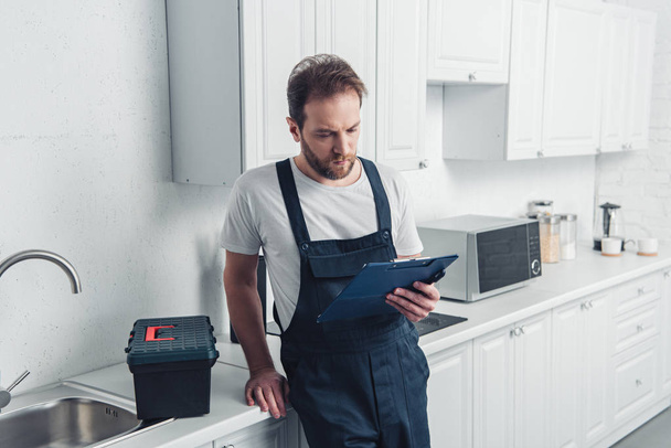 adult bearded repairman looking at clipboard in kitchen at home - Photo, Image