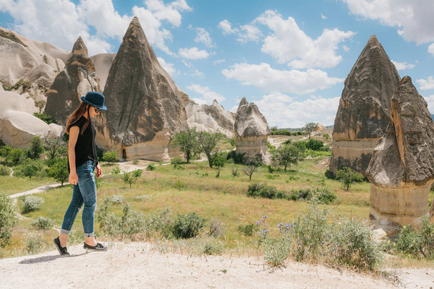 Девушка-туристка идет по дороге рядом с чудесными горками Каппечии в Турции и восхищается красотой вокруг. Пейзаж Каппадокии
. - Фото, изображение