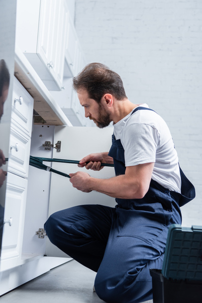 reparador enfocado en trabajar fregadero de fijación general con un par de pinzas en la cocina
  - Foto, imagen