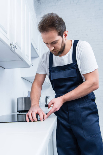 focused handyman in working overall fixing oven in kitchen - Foto, Imagen