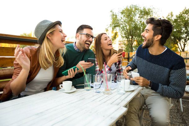 Skupina čtyř přátel společně baví na kávu. Dvě ženy a dva muži v kavárně mluvit, smát a užívat svůj čas. Používání telefonu  - Fotografie, Obrázek
