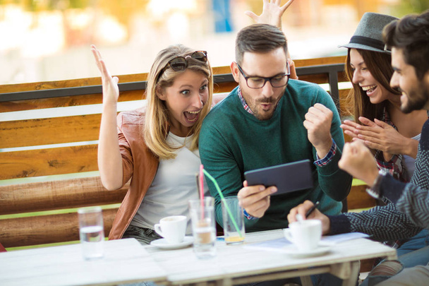 Grupa czterech przyjaciół razem mając na kawę. Dwie kobiety i dwóch mężczyzn w kawiarni, rozmawiając, śmiejąc się i cieszyć się ich czas za pomocą cyfrowego tabletu. - Zdjęcie, obraz