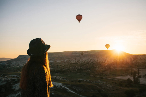 Şapkalı bir turist kız sıcak hava balonları Türkiye Kapadokya'da üzerinde gökyüzünde uçan hayran. Etkileyici görüş. - Fotoğraf, Görsel