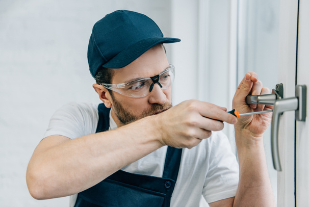 craftsman in goggles fixing window handle with screwdriver  - Фото, зображення