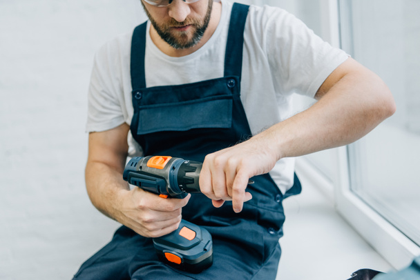 partial view of male handyman with electric drill sitting on windowsill  - Photo, Image