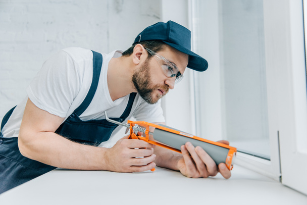 concentrated adult repairman fixing window with sealant gun - Foto, imagen