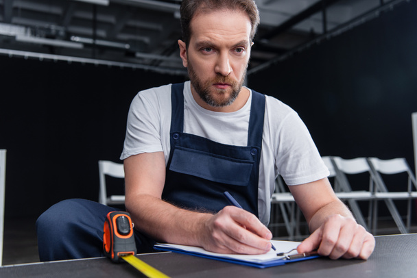 serious male handyman making measurements and writing in clipboard - Photo, Image