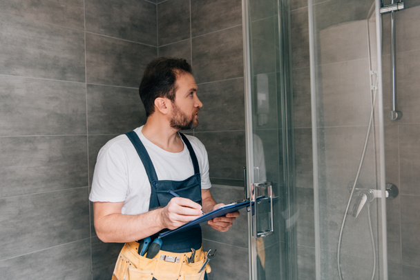 adult male plumber making notes in clipboard while checking shower in bathroom - Фото, зображення