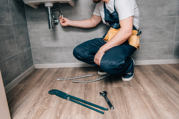 cropped shot of male plumber with toolbelt repairing sink in bathroom  - Фото, изображение