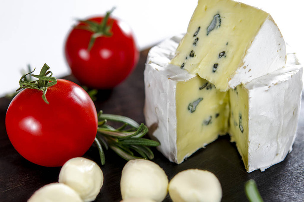 Assorted cheeses on wooden board. Camembert, cheese with blue mildew, mozzarella with tomatoes and rosemary - Photo, Image