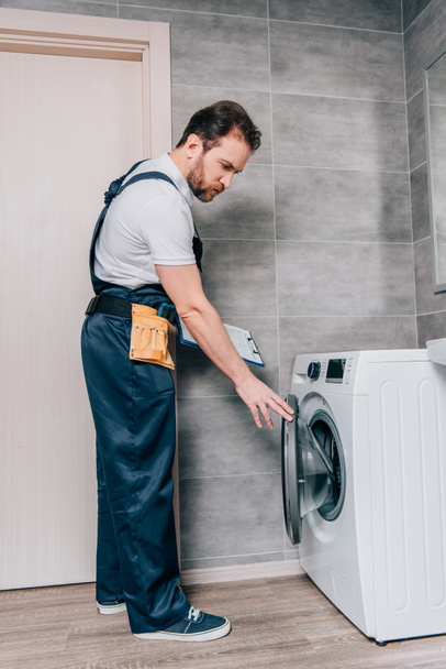 мужчина ремонтник с ремнем и буфером проверки стиральная машина в ванной комнате
 - Фото, изображение