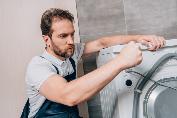 confident male handyman repairing washing machine in bathroom - Foto, imagen