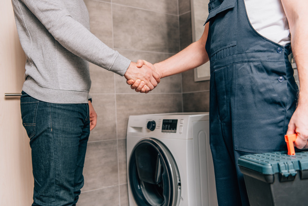 cropped image of male handyman with toolbox shaking hands with owner in bathroom - 写真・画像