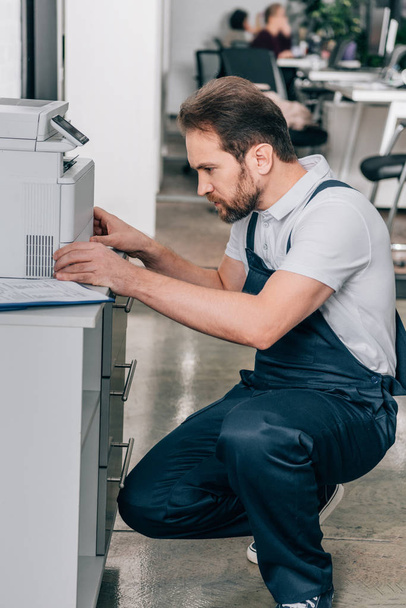 side view of male handyman repairing copy machine in modern office  - Valokuva, kuva