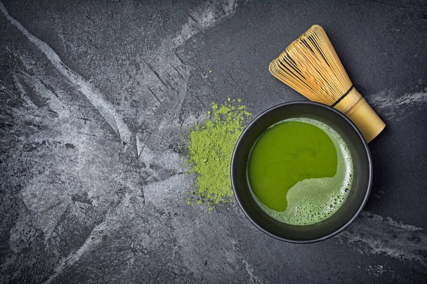 Top view on organic green matcha tea in ceramic cup with bamboo whisk on black marble background with copy space - Valokuva, kuva