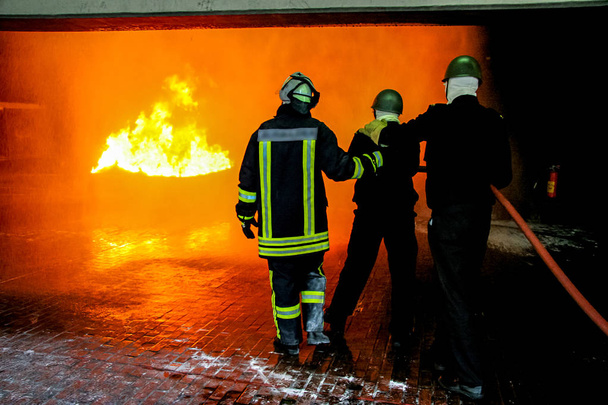 Πυροσβέστες κατάρτισης για πυρόσβεση στη Γερμανία. Πυροσβέστης σε Πυροσβεστική κοστούμι προστασίας ψεκασμό με νερό στη φωτιά με καπνό. Πυροσβέστης καταπολέμηση πυρκαγιάς επίθεση, κατά τη διάρκεια της κατάρτισης άσκηση - Φωτογραφία, εικόνα