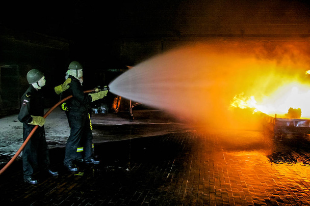 Bombeiros treinando para combate a incêndios na Alemanha. Bombeiro em terno de proteção contra incêndio pulverizando água para disparar com fumaça. Bombeiro combatendo ataque de fogo, durante exercício de treinamento
 - Foto, Imagem