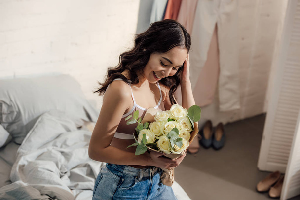 beautiful happy young asian woman holding bouquet of white roses in bedroom - Foto, afbeelding