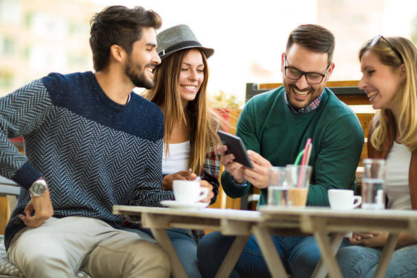 Groupe de quatre amis prenant un café ensemble. Deux femmes et deux hommes au café parlent en riant et apprécient leur temps en utilisant une tablette numérique
. - Photo, image