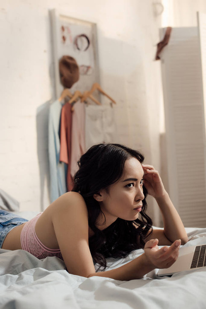 serious asian girl using laptop in bedroom - Photo, Image