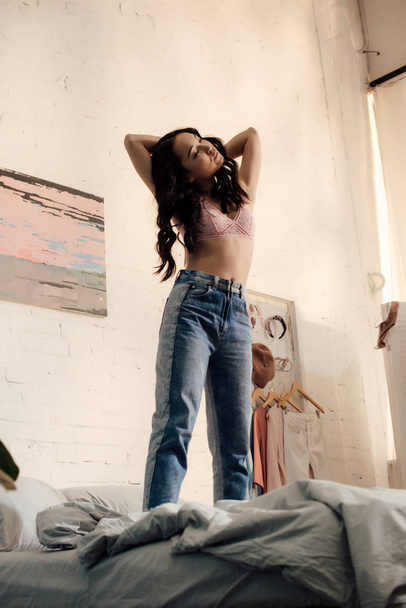 beautiful young asian woman in pink bra and jeans standing on bed - Fotografie, Obrázek