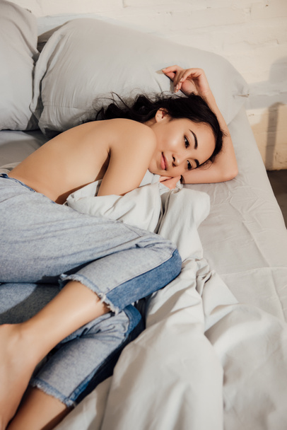 beautiful smiling young asian woman in denim pants lying on bed ta home - Fotoğraf, Görsel