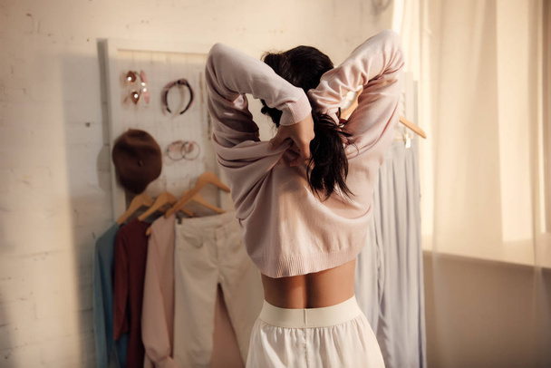 back view of young woman putting on stylish sweater at home  - Foto, afbeelding
