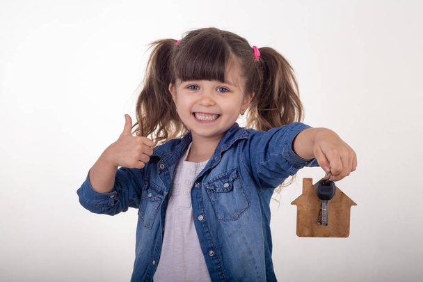 Μπράβο το παιδί κρατώντας σπίτι κλειδιά στο σπίτι σε σχήμα μπρελόκ σαν κτηματομεσίτη και δείχνοντας. - Φωτογραφία, εικόνα