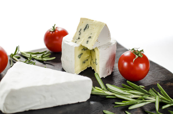 Assorted cheeses on wooden board. Camembert, cheese with blue mildew, mozzarella with tomatoes and rosemary - Photo, Image