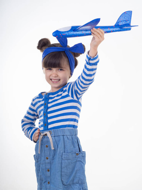 Mooi kind dragen gestreepte jurk blauw vliegtuigen te houden. Geïsoleerde, kopieer ruimte. Zomervakantie en lucht reizen concept.  - Foto, afbeelding