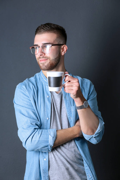 Portrait of a handsome young man standing and holding a cup of coffee in his hands - Foto, Bild