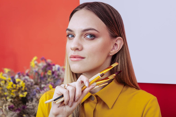 Portrait of appealing blonde-haired artist holding painting brushes - Foto, Imagem