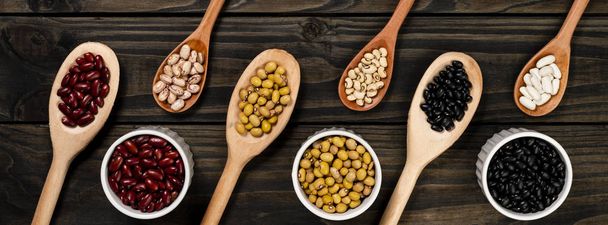 Diversity of beans inside wooden spoons. Black wood background. - Zdjęcie, obraz