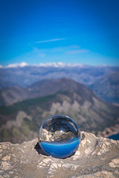 Stunning landscape of the Bay of Kotor and Lovcen National Park in Montenegro reflected in a large glass ball placed on a large boulder - Photo, Image