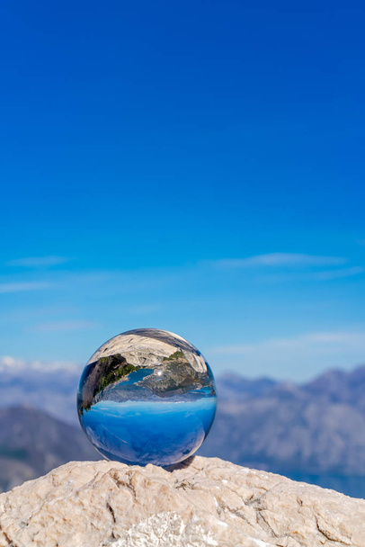 Stunning landscape of the Bay of Kotor and Lovcen National Park in Montenegro reflected in a large glass ball placed on a large boulder - Foto, afbeelding