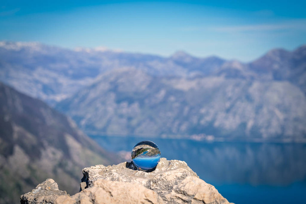 Atemberaubende Landschaft der Bucht von Kotor und des Nationalparks Lovcen in Montenegro, die sich in einer großen Glaskugel auf einem großen Felsbrocken widerspiegelt - Foto, Bild