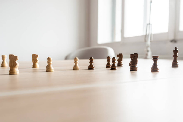 Black and white chess pieces teamed up and facing each other on a wooden office desk in a conceptual image of business competition. - Photo, Image