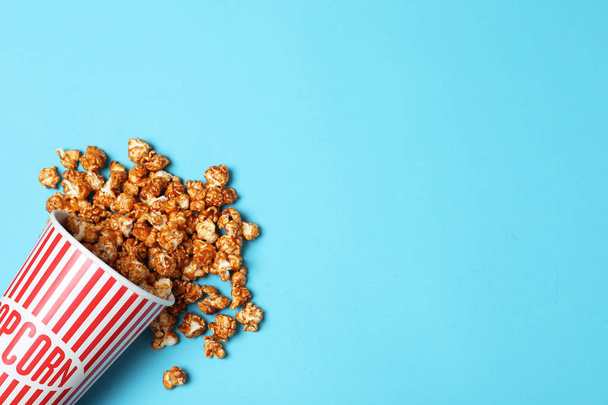 Overturned paper cup with caramel popcorn on color background, top view. Space for text - Фото, изображение