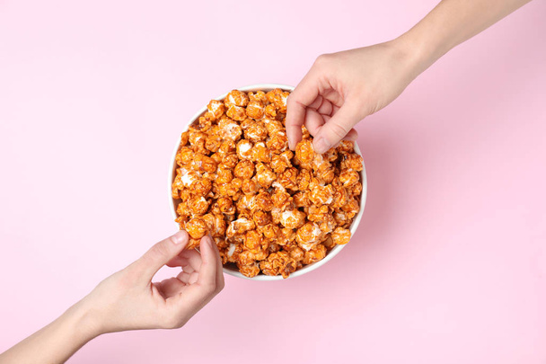 Women eating tasty popcorn from paper bucket on color background, top view - Fotoğraf, Görsel