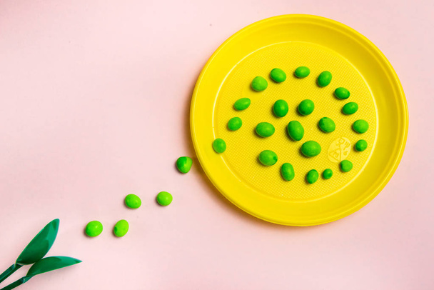 Gelber Plastikteller mit einem Pfad von Süßigkeiten mit grünen Löffeln auf rosa Hintergrund - Foto, Bild