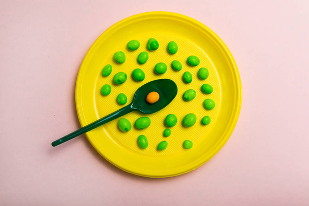 A yellow plastic plate filled with candy with a green spoon on a pink background - Photo, Image