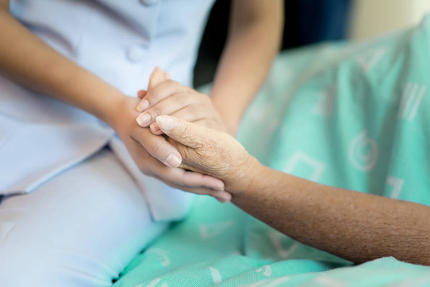 Nurse sitting on a hospital bed next to an older woman helping hands, care for the elderly concept - Photo, Image
