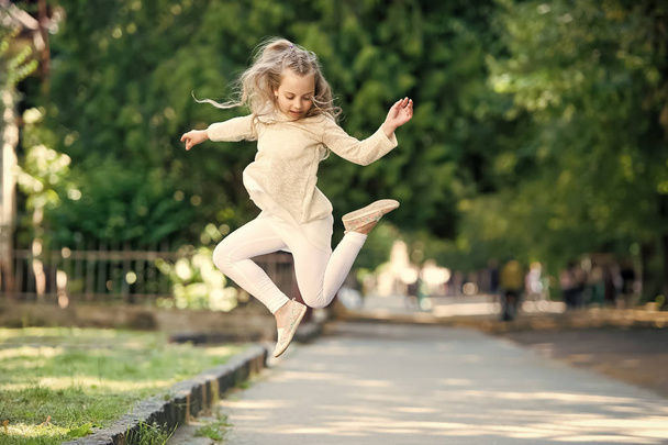 Pretty little girl with curly blonde hair jumping on street - Foto, Imagen