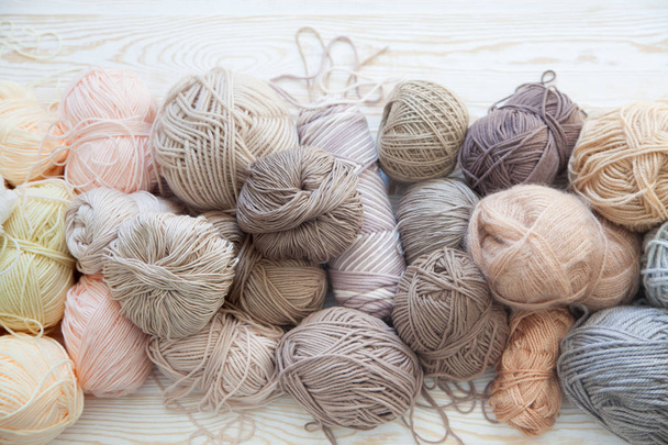 The yarn is beige, brown, gray and white. The background is aged wood. Knitting needles, scissors, coffee, knitting, knitted fabric. - Foto, afbeelding