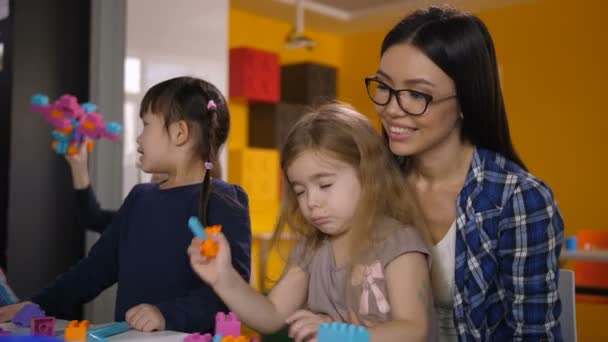 Carefree diverse multiracial children with preschool teacher having fun and playing with educational toys in kindergarten during playtime. Positive kids playing with colorful constrution toy blocks. - Footage, Video