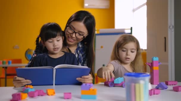 Preschool asian girl reading book with teacher - Footage, Video