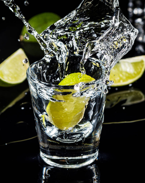 Mexican traditional  Tequila splash lime on black background with ice cube. - Fotó, kép