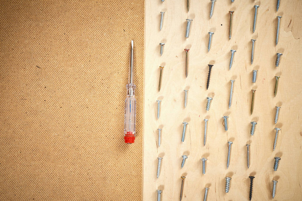 Musterhintergrund verschiedener Schrauben und Schraubenzieher auf einem hölzernen Arbeitstisch - Foto, Bild